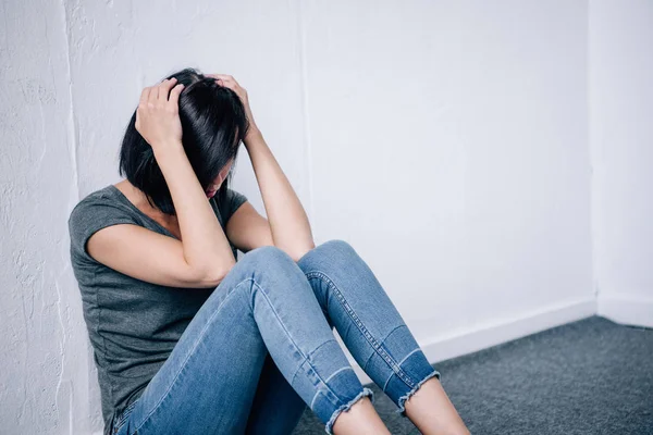 Депресивна брюнетка жінка з руками на голові сидить вдома — стокове фото
