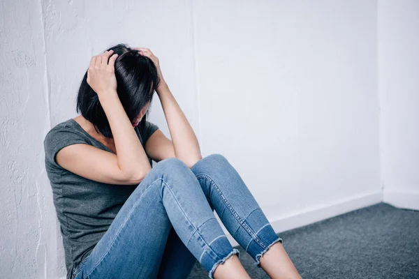 Femme brune déprimée avec les mains sur la tête assise à la maison — Photo de stock