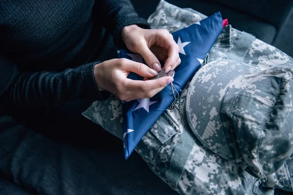 Vue recadrée de la femme sur le canapé avec des vêtements militaires, tag chien et drapeau américain foded à la maison — Photo de stock