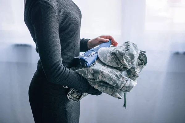 Vista ritagliata di donna che detiene abbigliamento militare a casa — Foto stock