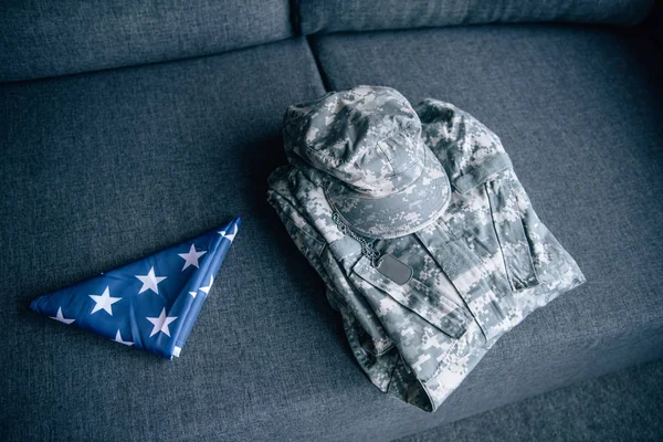 Military clothing and folded american flag on couch at home — Stock Photo