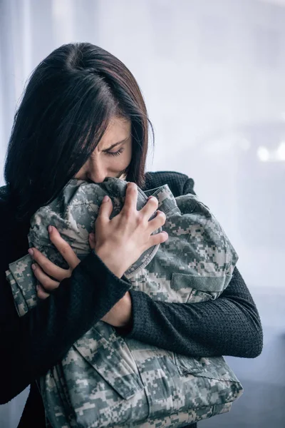 Depressed woman crying and holding military clothing at home — Stock Photo