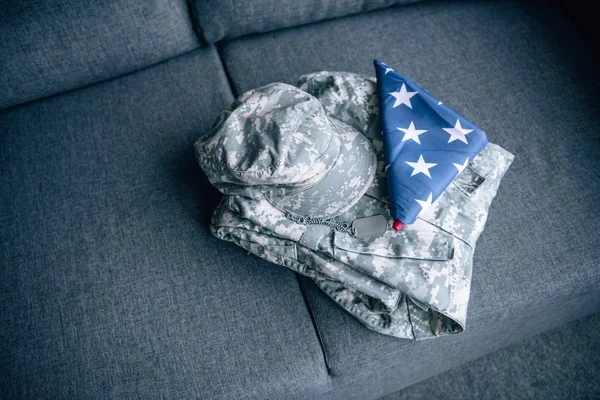 Military clothing and folded american flag on couch at home — Stock Photo