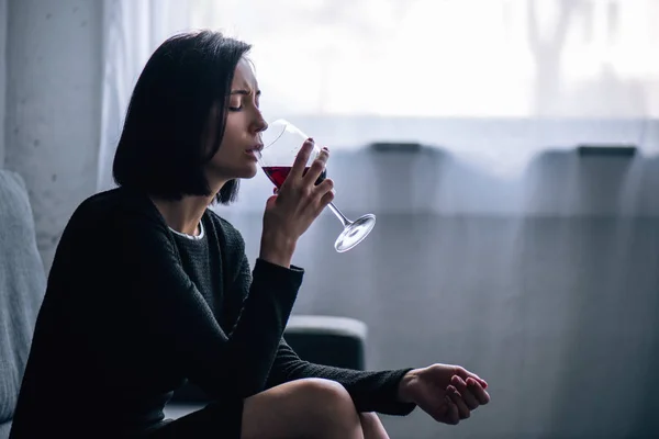 Femme seule déprimée assise sur le canapé et buvant du vin à la maison — Photo de stock