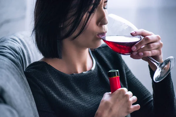 Depressed woman sitting on couch and drinking wine at home — Stock Photo