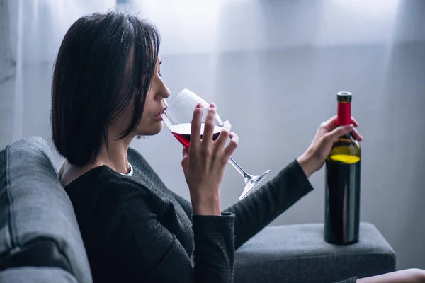 Depressed lonely woman sitting on couch and drinking wine at home — Stock Photo