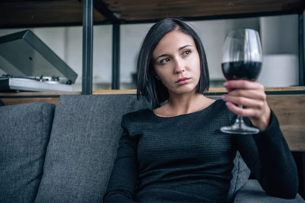 Depressed woman on couch looking at wine glass at home — Stock Photo