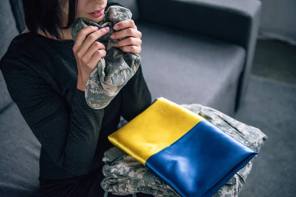 Vista ritagliata di donna sconvolta con abbigliamento militare e bandiera ucraina a casa — Foto stock