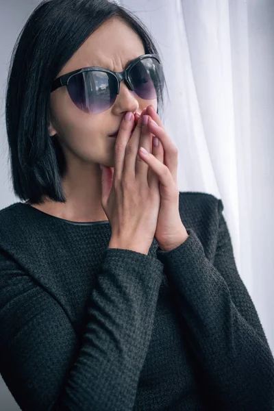 Depressed lonely woman in sunglasses covering mouth and grieving at home — Stock Photo