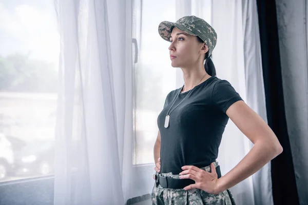 Bela mulher com mão no quadril em uniforme militar em casa com espaço de cópia — Fotografia de Stock