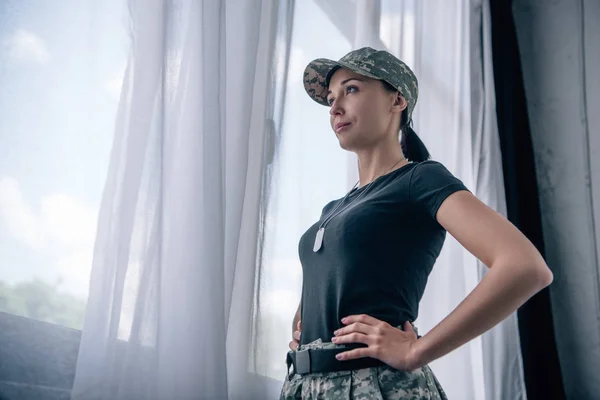 Mulher atraente com a mão no quadril em uniforme militar em casa com espaço de cópia — Fotografia de Stock
