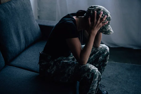 Mujer deprimida en uniforme militar con las manos en la cabeza en casa - foto de stock