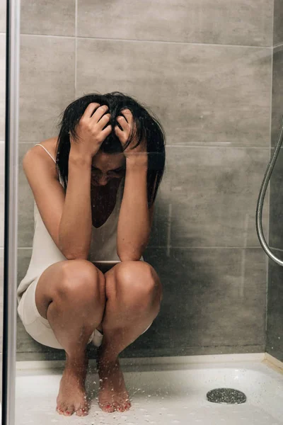 Одинокая депрессивная женщина с руками на голове сидит в душе дома — стоковое фото
