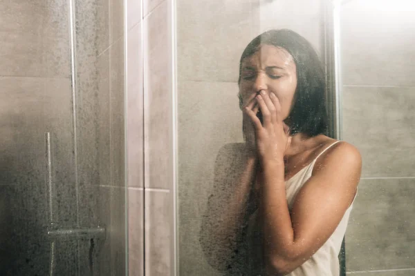Lonely depressed woman covering mouth and crying in shower at home — Stock Photo
