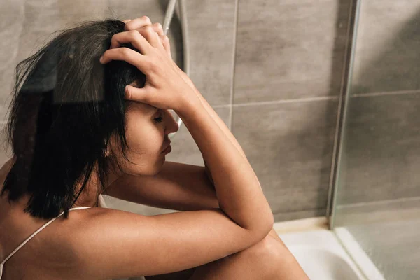 Einsame depressive Frau sitzt unter der Dusche und berührt zu Hause den Kopf — Stockfoto