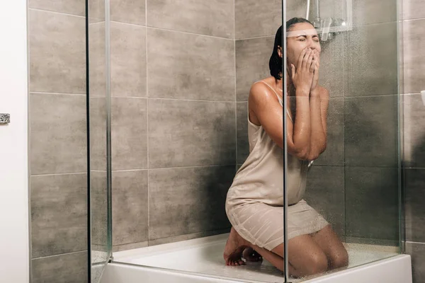 Lonely worried woman covering mouth while sitting in shower at home — Stock Photo