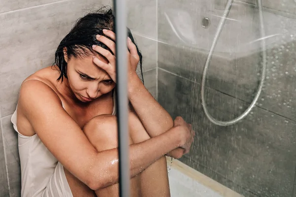 Einsame aufgebrachte Frau mit Hand auf dem Kopf, die zu Hause unter der Dusche sitzt — Stockfoto