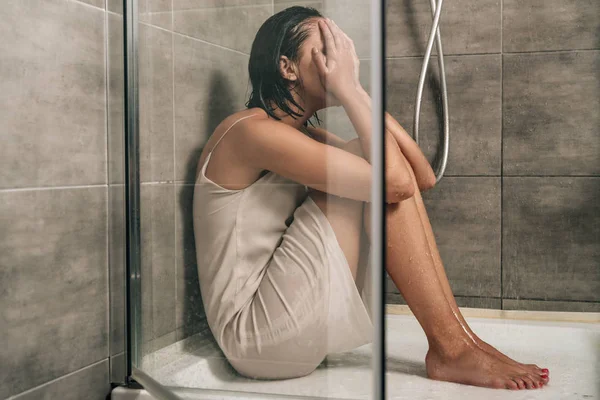 Triste mujer deprimida cubriendo la cara mientras se sienta en la ducha en casa - foto de stock