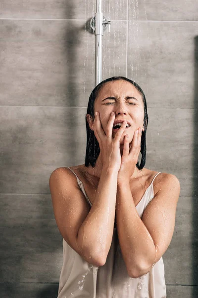 Donna solo depressa che copre la bocca con le mani mentre piange sotto la doccia a casa — Foto stock