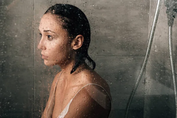 Hermosa mujer triste en la ducha en casa a través de vidrio con gotas de agua - foto de stock