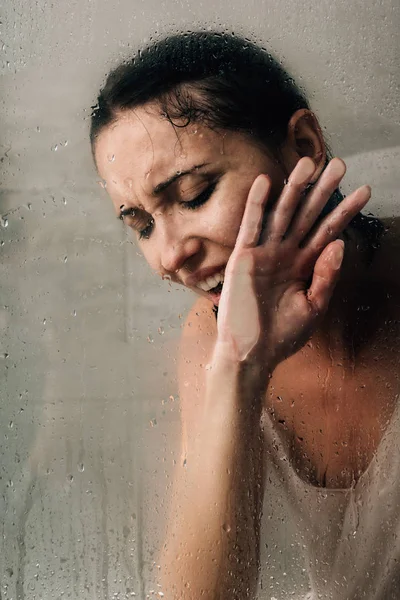 Femme déprimée solitaire pleurer dans la douche à travers le verre avec des gouttes d'eau — Photo de stock