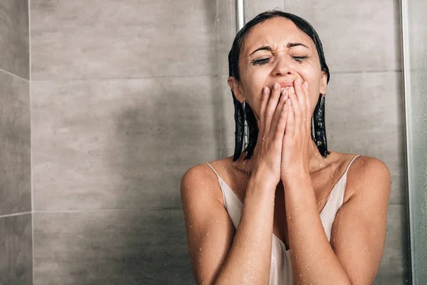 Mujer deprimida solitaria en la ducha cubriendo la boca y llorando en casa - foto de stock