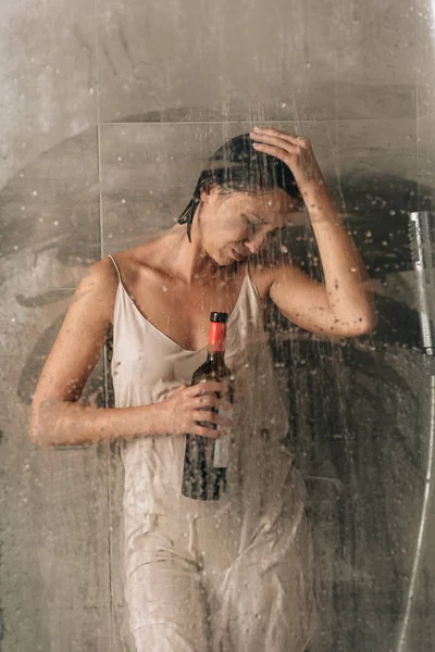 Depressed woman in shower holding wine bottle and crying at home — Stock Photo