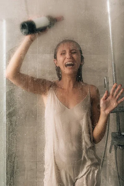 Mujer deprimida solitaria en la ducha sosteniendo botella de vino y llorando en casa - foto de stock