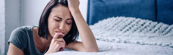 Tiro panorâmico de mulher morena deprimida chorando perto da cama em casa — Fotografia de Stock