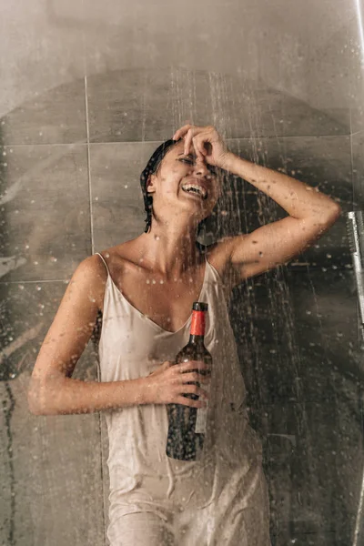 Lonely depressed woman in shower holding wine bottle and crying at home — Stock Photo