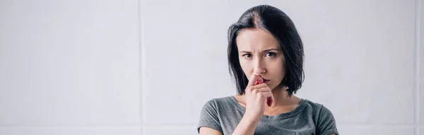 Plan panoramique de femme triste et coûteuse touchant le menton et regardant la caméra à la maison — Photo de stock