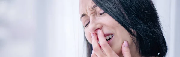 Tiro panorâmico de mulher morena deprimida chorando e cobrindo a boca em casa — Fotografia de Stock