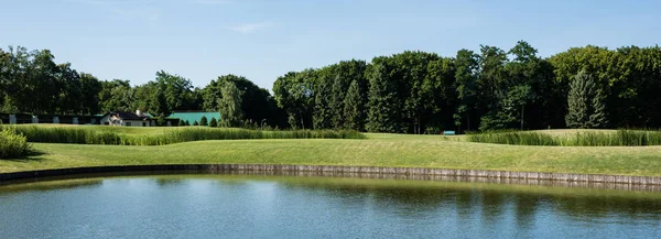 Panoramic shot of green trees near lake and blue sky with clouds — Stock Photo