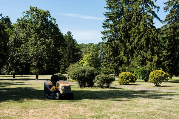 Cortador de grama na grama verde perto de sombras e árvores no parque — Fotografia de Stock