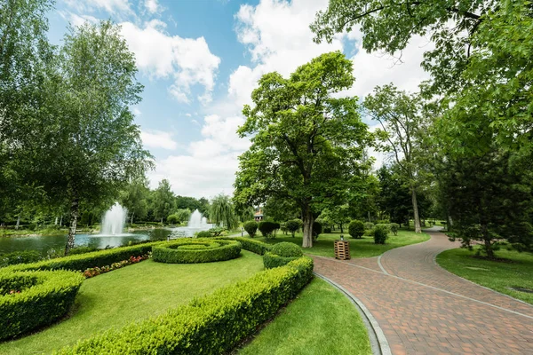 Walkway near green plants, trees and fountains against blue sky — Stock Photo