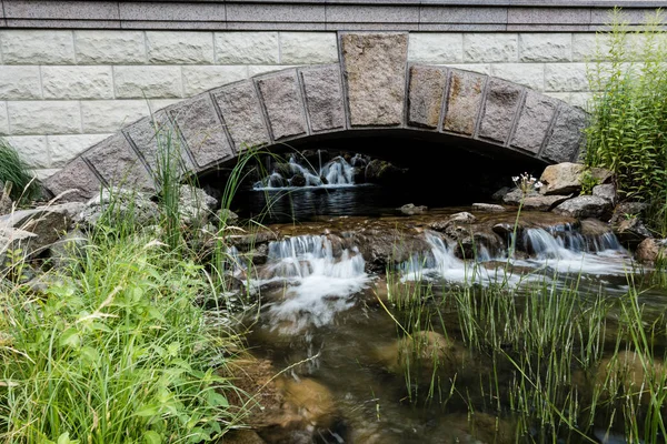 Puente de piedra cerca de vapor con agua que fluye sobre rocas en el parque - foto de stock