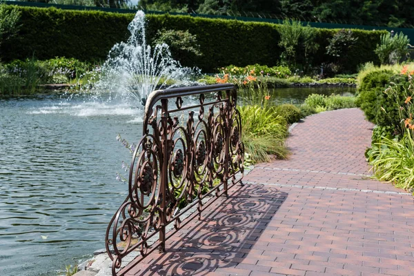 Selective focus of metallic fence on bridge near lake with fountain — Stock Photo