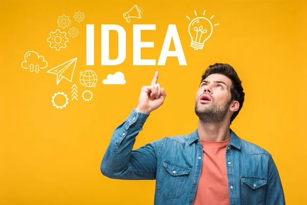Confused handsome man pointing with finger at idea lettering isolated on yellow — Stock Photo