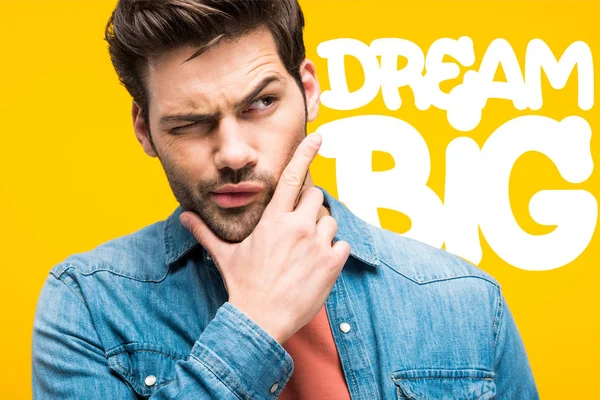 Hombre guapo reflexivo tocando la barbilla aislado en amarillo con gran inspiración sueño - foto de stock