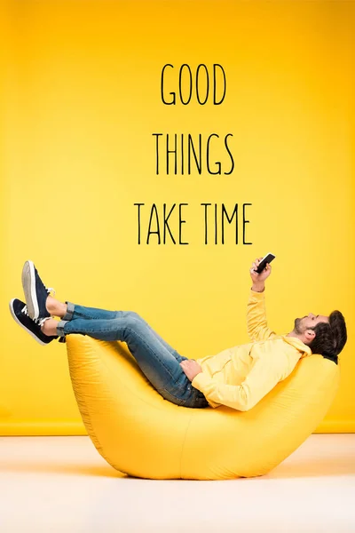 Hombre relajante en la silla de la bolsa de frijol y el uso de teléfono inteligente sobre fondo amarillo con cosas buenas toman tiempo inspiración - foto de stock