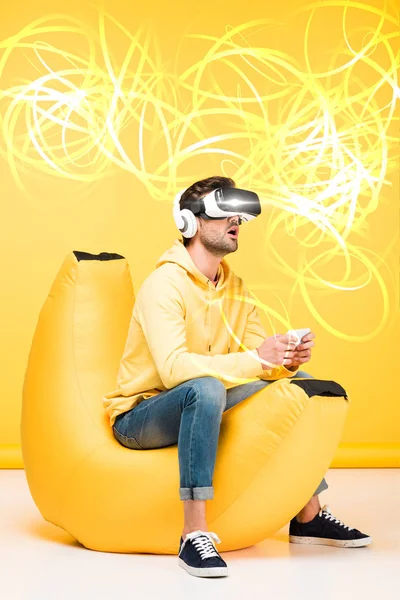 Excited man on bean bag chair in virtual reality headset on yellow with cyberspace illustration — Stock Photo