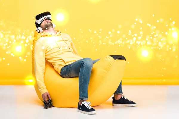 KYIV, UCRAINA - 12 APRILE: l'uomo dorme sulla sedia del sacchetto di banana bean con joystick in realtà virtuale auricolare su giallo con illustrazione ciberspazio — Foto stock