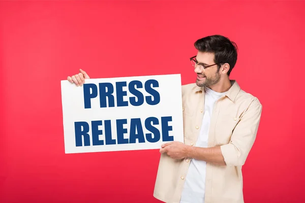 Homem bonito segurando cartaz branco com ilustração press release isolado em vermelho — Fotografia de Stock