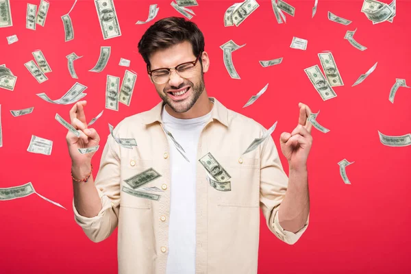 Handsome man with fingers crossed isolated on red with money rain illustration — Stock Photo