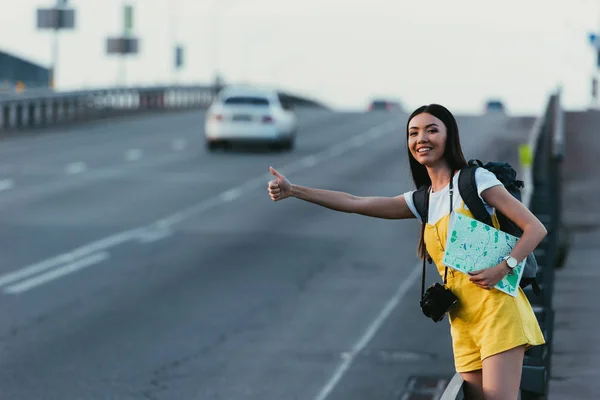 Asian woman in yellow overalls hitchhiking and holding map — Stock Photo