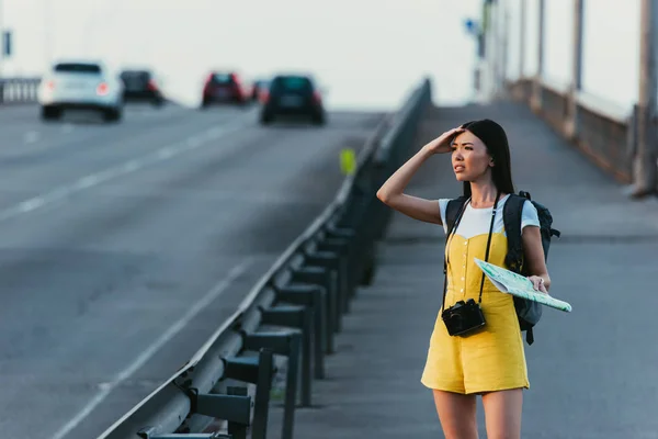 Besorgte und asiatische Frau in Overalls mit Landkarte und wegschauendem Blick — Stockfoto