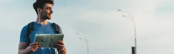 Plano panorámico de hombre sonriente y guapo en camiseta sosteniendo mapa - foto de stock