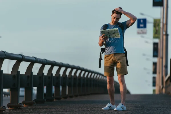 Homem triste e bonito em t-shirt e shorts olhando para o mapa — Fotografia de Stock