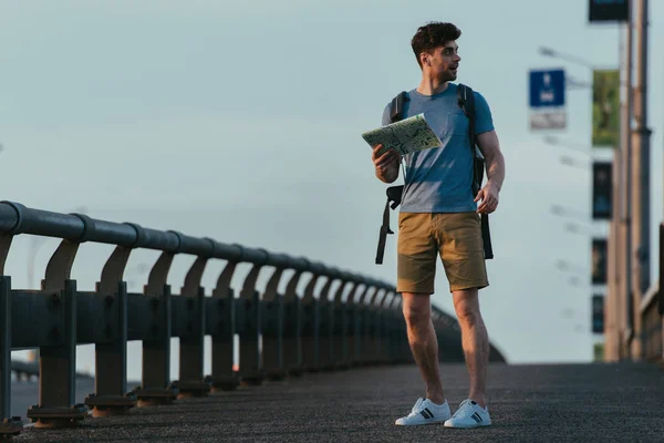 Homem bonito em t-shirt e shorts segurando mapa e olhando para longe — Fotografia de Stock