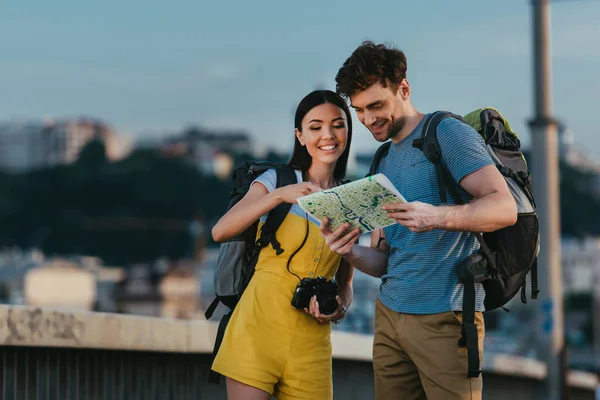 Guapo hombre y asiático mujer sonriendo y mirando mapa - foto de stock